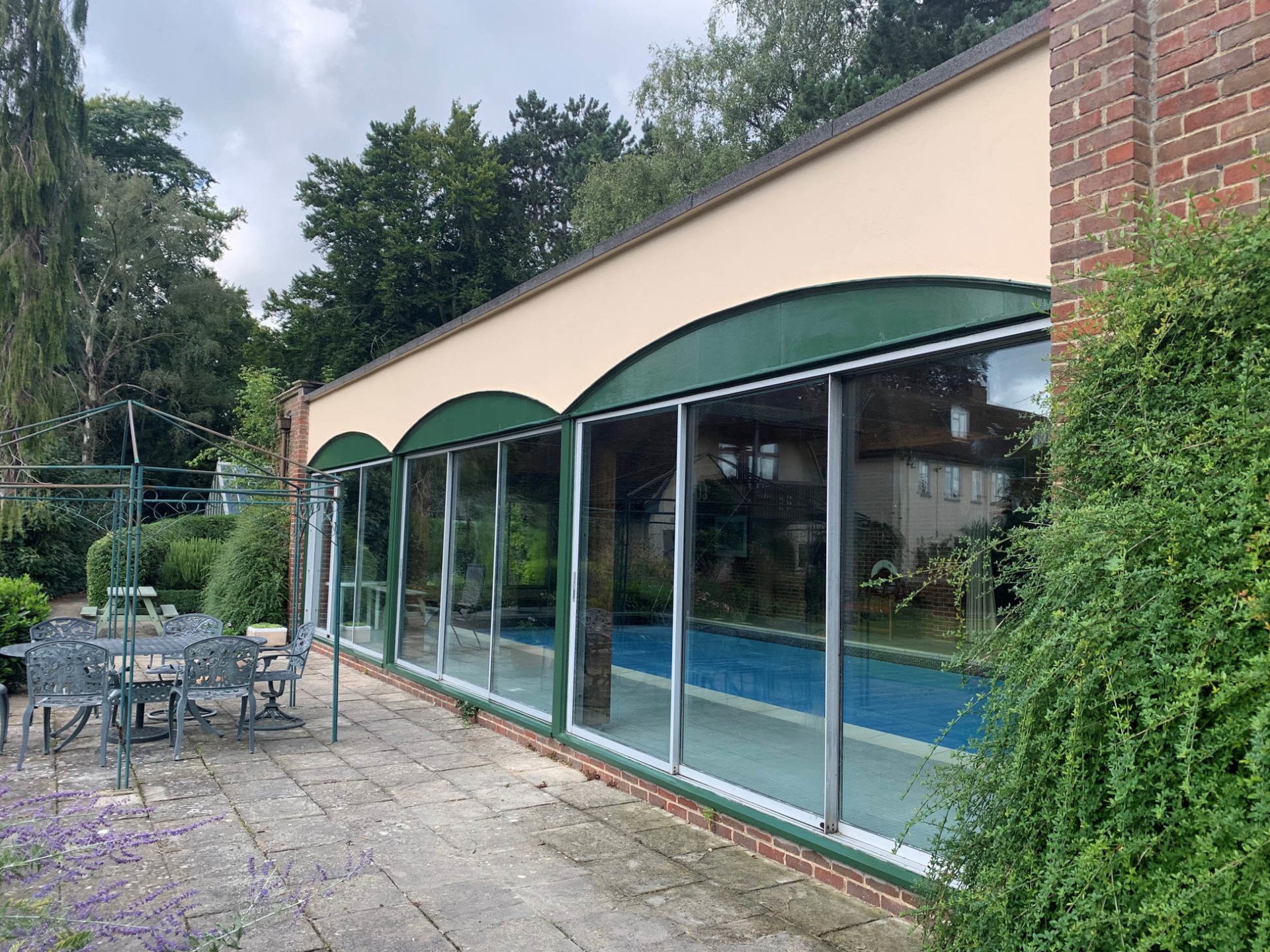 Pool house finished in cream with green arched glazing